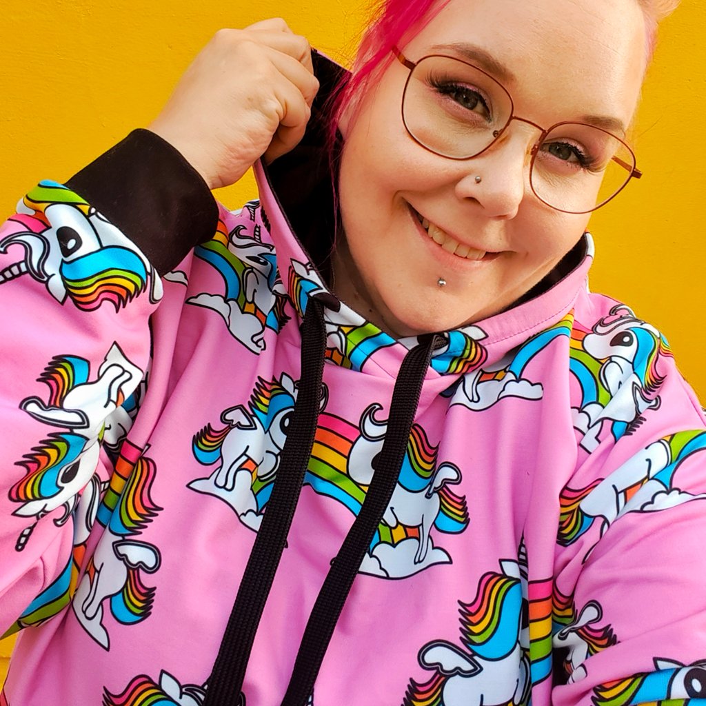 Lady in a colorful hoodie with a unicorn print in rainbow colors and pink background..