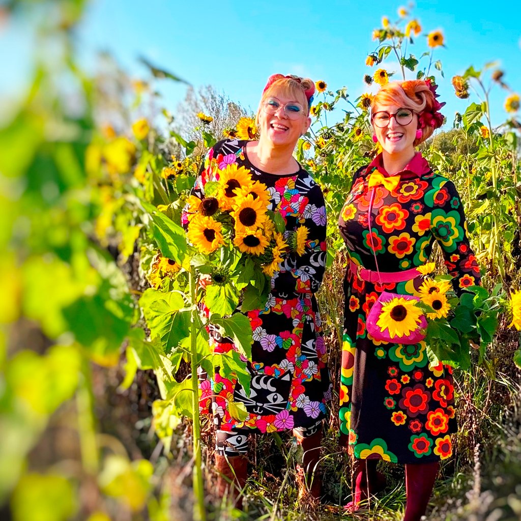 Two smiling women in colorful clothes among sunflowers.